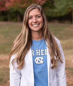 Dr. Dameworth in a white coat and blue shirt standing outdoors with trees in background.